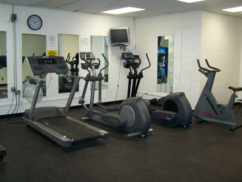 A well-lit indoor fitness room featuring various cardio equipment, including treadmills and exercise bikes.
